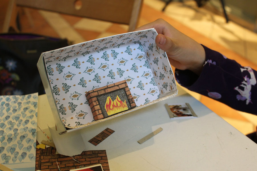 Diorama w wykonaniu uczestniczki warsztatów. Małe pudełeczko wyklejone w środku wzorzystym papierem, dodatkowo naklejone mniejsze pudełko imitujące kominek.